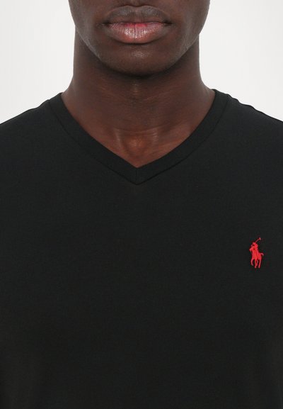 Melnā V veida t-krekls, kas izgatavots no mīkstas auduma, ar mazu sarkanu polo logotipu kreisajā krūšu zonā. Brīvs dizains ar ērtu piegriezumu.