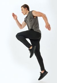 Mannelijke sportkleding in een grijze mouwloze top en zwarte fitted broek, beide met een gladde textuur. Zwarte hardloopschoenen hebben gestructureerde zolen.