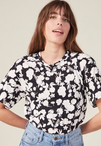 Camiseta negra con patrón floral blanco, de manga corta, cuello redondo y textura suave, combinada con pantalones cortos de denim azul de cintura alta.