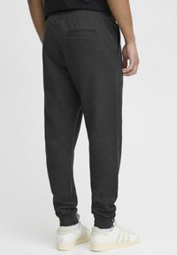 Mørkegrå sweatpants lavet af blødt stof med elastiske manchetter, en baglomme og en tapered design. Sammen med hvide sneakers.