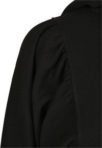 Top nero con un tessuto testurizzato e dettagli arricciati nella spalla. Il design ha un aspetto liscio e aderente.