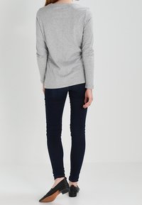 Graues Langarmshirt kombiniert mit dunkelblauen Skinny-Jeans und schwarzen Ballerinas, mit einem schlichten Design und taillierten Formen.
