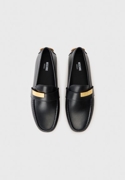 Svarta läderloafers med en guldfärgad accentband. Slät textur, rund tå, utan snörning, med varumärkeslogotyp på innersulan.