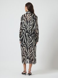 Mulher de costas, vestindo um vestido midi de mangas compridas com estampa abstracta de zebra em preto e bege, e sandálias pretas de salto alto.