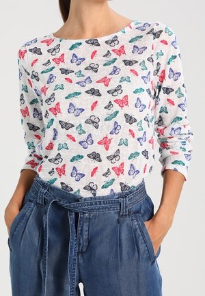 Langærmet skjorte i hvidt stof med et sommerfugleprint i sort, rød, blå og grøn. Kombineret med højtaljede denimbukser.