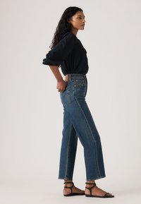 Τζιν παντελόνι μέσης ψηλής με φαρδιές γραμμές, πλαϊνές σχισμές και ταμπά ζώνη. Συνδυασμένο με μαύρο, μακρυμάνικο τοπ και μαύρα σανδάλια.