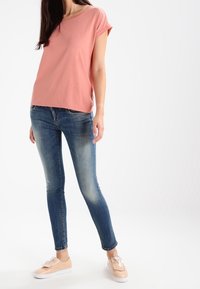 Ljusrosa kortärmad topp i kombination med åtsittande blå jeans och beige sneakers med snördetaljer. Slät tyg och avslappnad passform.