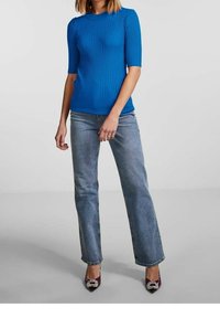 Modré žebrované tričko s krátkým rukávem spárované se světle modrými džíny rovného střihu. Obuv zahrnuje fialové lodičky s dekorativními akcenty.