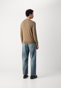 Bruine langemouwen trui met een aangesloten kraag, gecombineerd met losse lichtblauwe jeans met achterzakken en zwarte schoenen.