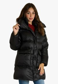 Giacca imbottita nera con colletto alto, molteplici tasche frontali e texture lucida. Sono visibili bottoni e dettagli di cucitura.