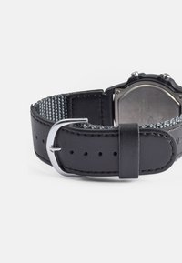 Pulseira de relógio em couro preto com forro de tecido cinza texturizado, fivela prateada e orifícios visíveis para ajuste. Parte traseira metálica do relógio é parcialmente visível.