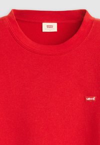 Felpa in cotone rossa con collo a girocollo a costine. Presenta una piccola etichetta bianca con il logo Levi's sul lato sinistro del petto. Texture morbida.