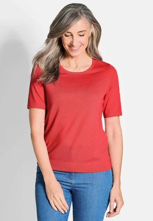 Rotes kurzärmliges Strickoberteil mit Rundhalsausschnitt; glatte Textur, schlanke Passform und gerippten Saum, kombiniert mit blauen Jeans.