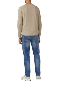 Beiges Langarmhemd mit Raglanärmeln, kombiniert mit hellblauen Jeans. Die Person trägt weiße Turnschuhe mit grünen Akzenten.