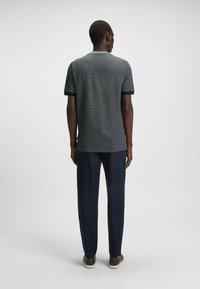 Maglietta grigia a maniche corte con accenti neri, realizzata in tessuto testurizzato, abbinata a pantaloni scuri e sneakers neutre.