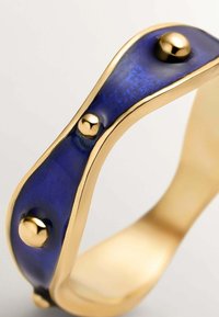 Anillo de oro con banda ondulada que presenta una franja de esmalte azul profundo adornada con tres tachuelas de oro pulido distribuidas uniformemente.