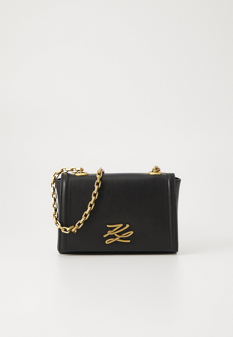 Black leather handbag with a structured design, gold chain strap, and a bold logo accent on the front. Features a smooth texture.