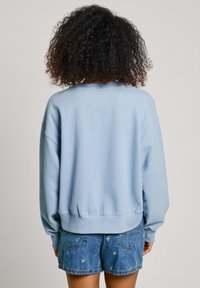 Lichtblauwe sweatshirt met lange mouwen, ribgebreide manchetten en onderzoom. Gecombineerd met denim shorts met kleine geborduurde details.
