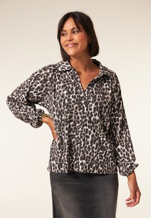 Zwart-witte luipaardprint blouse met een kraag, lange mouwen en een ontspannen pasvorm, vergezeld van een grijze spijkerrok.