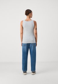 Sivý, priliehavý tank top vyrobený z bavlny, s okrúhlym výstrihom a bezrukávovým dizajnom, skombinovaný s voľnými modrými džínsami.