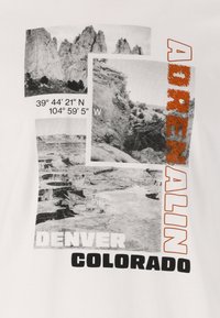 Vit t-shirt med svarta och grå landskapsfotografier, texten "ADRENALIN," "DENVER," och "COLORADO" i fet orange och svarta typsnitt.