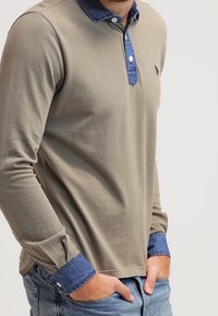 Polo à manches longues en vert olive avec un col et des poignets en denim, doté d'une patte de boutonnage et d'un logo discret sur la poitrine.