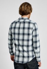 Mäns långärmad flanellskjorta i blå och vit rutigt mönster. Har en spetsig krage och knäppningar vid ärmarna, med en mjuk textur och rundad fåll.