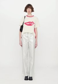 Cream t-shirt with red lips print, paired with silver metallic wide-leg pants. Black crossbody bag and black shoes complete the outfit.