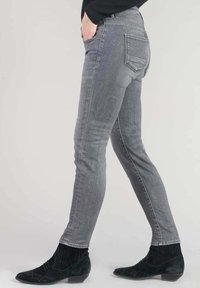 Jean en denim gris skinny avec une texture lisse, taille mi-haute et design à cinq poches, assorti à des bottines noires à la surface texturée.