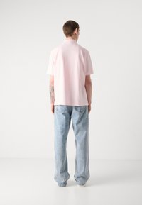 Polo shirt rose clair à manches courtes, texture lisse et col ouvert, associé à un jean bleu clair ample.