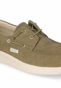 Scarpa in suede color oliva chiaro con punta arrotondata, lacci decorativi e suola in gomma a contrasto. Presenta un piccolo logo sul lato.