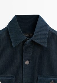 Camicia in corduroy blu scuro con colletto, caratterizzata da righe verticali e chiusura con bottoni. L'etichetta riporta "Massimo Dutti". La texture è morbida.