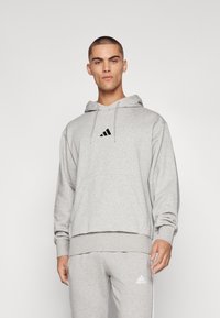 Hoodie cinza claro feito de tecido suave, apresentando um bolso frontal, capuz com cordão e um logo preto da Adidas no peito.