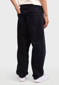 Black denim pants with a relaxed fit, featuring back pockets and a visible waistband, paired with white sneakers.