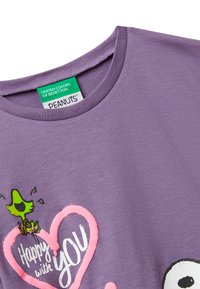 Fialová košile s růžovým srdcem a zeleným kresleným ptáčkem nad bílým textem "Šťastný s tebou," s etiketou United Colors of Benetton Peanuts.