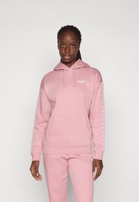 Rosa hettegenser laget av mykt stoff med kengurulomme, med en liten logo på brystet og mønstrete detaljer langs ermene.