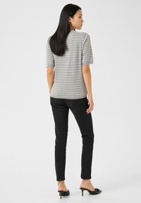 Hallide triibuline lühikeste varrukatega topp, mille lõige on vaba, kombineeritud mustade kitsaste pükstega ja avatud kannaga kontsadega. Siidine tekstuur ja vabaaja stiil.