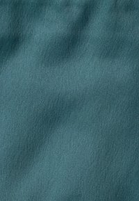 Teal, teksturoitu kangas, jossa on hienovarainen kiilto, joka sisältää sileän pinnan ja kevyet laineet, viitaten pehmeyteen ja sulavuuteen.