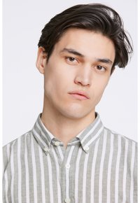 Camisa de botones con rayas verticales verdes y blancas, hecha de una tela ligera. Presenta un cuello y botones blancos.