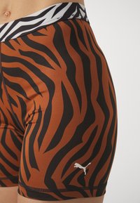 Pantaloni da atletica a strisce tigre marroni e neri con un elastico bianco in vita e un piccolo logo Puma bianco sul lato sinistro in basso.