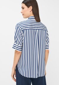 Blusa a righe blu e bianche con maniche corte, vestibilità aderente, dettaglio sulla spalla posteriore e orlo curvo per un aspetto rilassato.