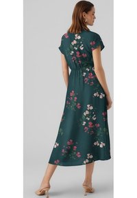 Robe imprimée florale en vert foncé avec des manches courtes, une taille élastique et une longueur midi fluide. Présente des fleurs roses et blanches.