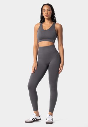 Gray athletic crop top and high-waisted leggings made of stretchy, smooth material. Model wears gray and white sneakers with black stripes.