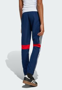 Marina träningsbyxor med röd rand, elastisk midja, vita sidostripes och ankle cuffs. Bärs med svarta skor med vita ränder.