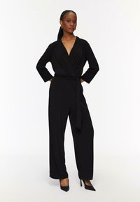 Czarny kombinezon w stylu owijanym z długimi rękawami, dekoltem w kształcie litery V i pasa z paskiem. Gładki materiał i szerokie nogawki z dopasowanymi mankietami.