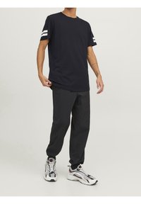 Marinblå bomullströja med vita ränder på ärmarna, ihop med svarta smala byxor och vit-grå sportskor. Enkelt, avslappnat outfit.