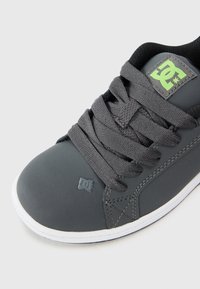 Šedá skate obuv vyrobená z gumy a textilu, s polstrovaným jazykem, texturovanými tkaničkami a texturovanou značkovou nášivkou v zelené barvě. Bílá podrážka.