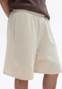 Beige Textur-Shorts mit lockerer Passform, ausgestattet mit einem bequemen elastischen Bund, Seitentaschen und einem knielangen Schnitt.