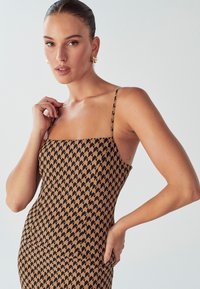 Hnedé vzorované šaty so štvorcovým výstrihom, tenkými ramienkami a priliehavým strihom, zdobené geometrickým vzorom v čiernej farbe.