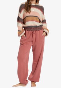 Gestrickter gestreifter Pullover in Creme-, Rosa- und Brauntönen; kombiniert mit locker sitzenden Sweatpants in Staubrosa mit elastischem Bund und Taschen.